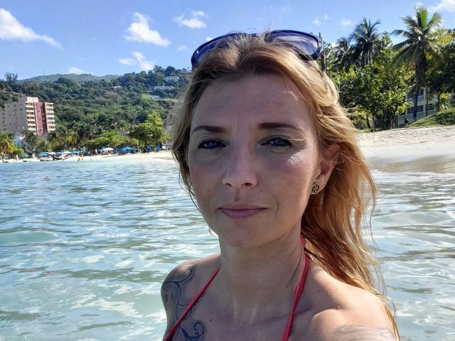 AbenteuerMelody-hot with blonde hair, blue eyes, and small tits in a red bikini top, standing in clear water, wearing sunglasses on her head, showing a tattoo on her right shoulder.
