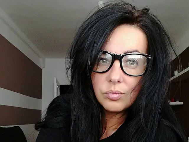 Lenore-hot with black hair, glasses, and pouty lips, wearing a black shirt, has a fair skin tone and is making a silly face. Boobs not visible.