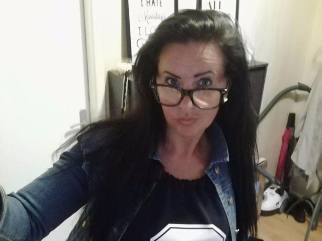Lenore-hot with long black hair, wearing glasses, a denim jacket, and a black and white shirt, pouting slightly. Her blue eyes are visible, and she's taking a selfie.