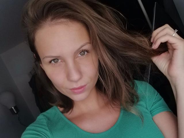 MaryWet-hot with light brown hair, green eyes, and a slight smile, wearing a green shirt, touching her hair with a ringed hand, showing a cute, attractive face.