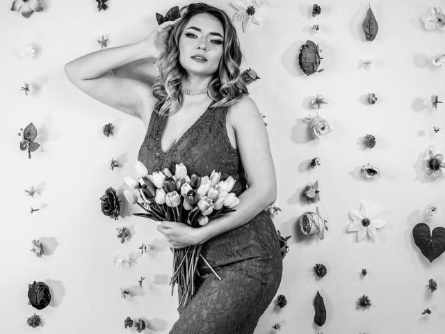SallyVerda with wavy blonde hair, wearing a lace dress, holding a bouquet of tulips, standing, hand in hair, looking at camera, black-and-white photo, full figure, sexy.