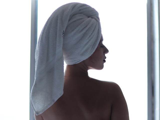 ValeryScot's back is to the camera, with a white towel wrapped around her head, showing bare shoulders and a side profile. Her face is partially shadowed.