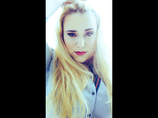 HaileyBLONDE-hot with long blonde hair, wearing a striped shirt, raising her arm, showing off her tits, with red lipstick and subtle makeup, in a bright photo.