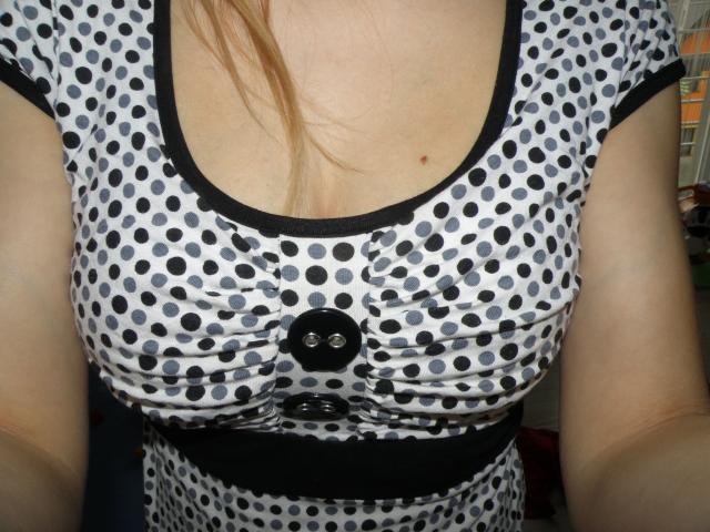 NNataszka-hot's polka-dotted dress with black buttons, showing her tits, has a black trim and a belt under her bust, with blonde hair falling over her chest.