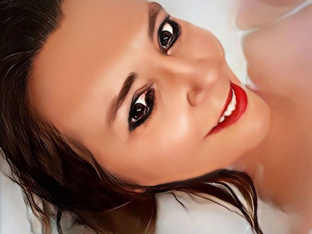Simone-69 has wet brown hair, red lipstick, and black eyeliner, smiling with shiny skin and visible white teeth in a bath. Her eyes are dark and slightly upturned.