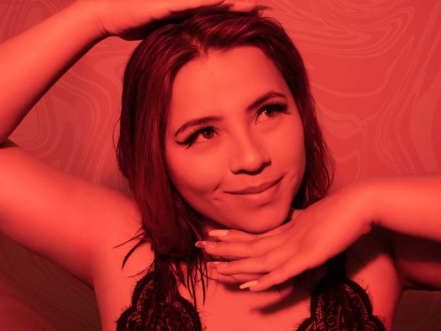 MelisaBrunette with red-tinted skin, dark lace top, wet shoulder-length hair, hands on neck, subtle smile, looking to the side, showing off her tits.