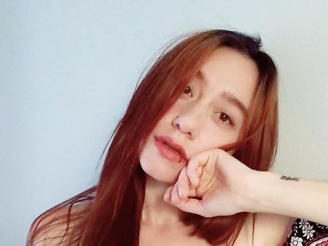 NutI a de longs cheveux roux, un anneau au nez, et repose son menton sur sa main avec une légère moue. Ses yeux sont marron, et elle a un tatouage au poignet..