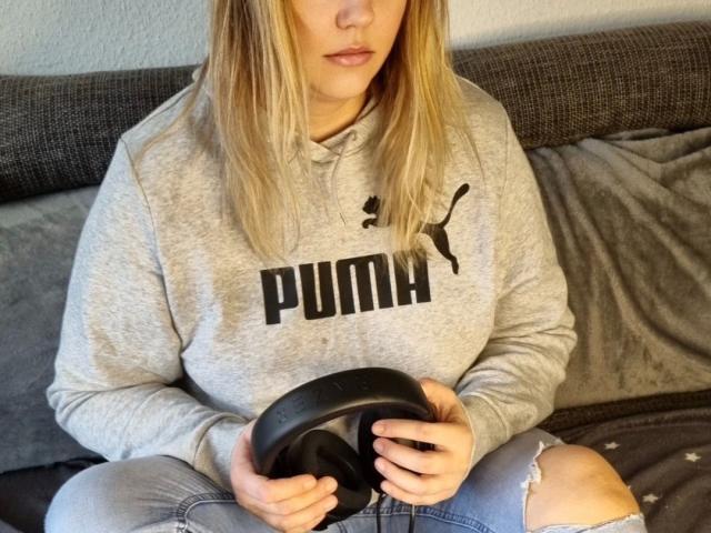 LiesaBDSM-hot with blonde hair, wearing a gray Puma hoodie, holding a black gaming controller, sitting on a gray couch, with slightly ripped jeans.