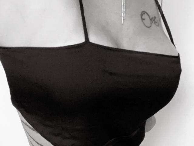 LesLioups' black tank top is pulled tight over her sizable tits, showing a tattoo on her upper chest. Her skin is light, and the tank top is slim.