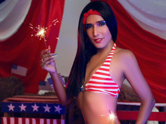 FallonRogers mit langem, schwarzem Haar, einem roten Stirnband, einem gestreiften roten-weißen Bikini, die einen Funkenstecher hält, lächelt und kleine Brüste zeigt, schlank, attraktiv, in einem patriotisch gestalteten Arrangement..