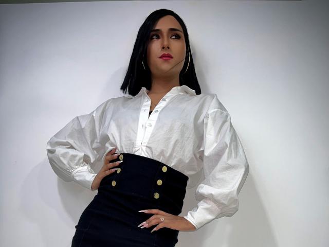 FallonRogers with black hair, white puffy shirt, black high-waisted skirt with gold buttons, hands on hips, looking to the side, wearing hoop earrings and pink lipstick.