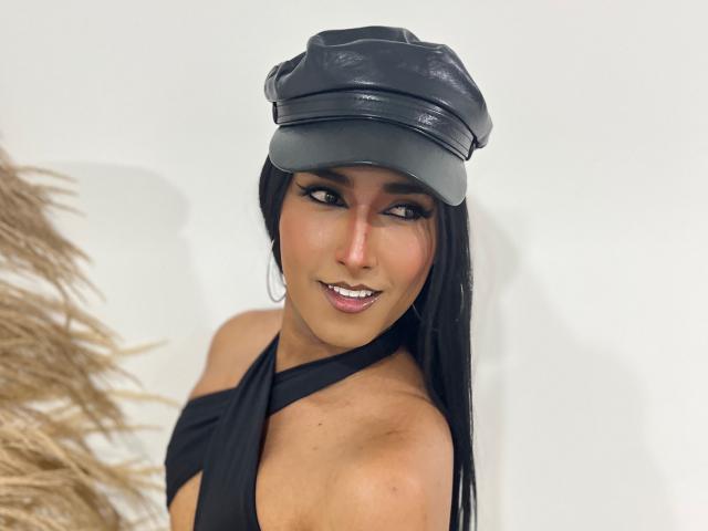 FallonRogers with long black hair, wearing a black leather cap and a halter black top, showing off her tits and a cute smile. Her eyes are seductive and she's sexy.