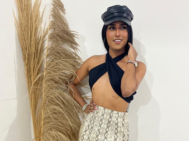 FallonRogers with a black cap, wearing a halter top that exposes her small tits and a snake-pattern skirt, standing next to tall, dry pampas grass.