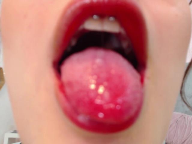 KimSummer's red-lipped mouth is open with her tongue out, showing a shiny, wet, pink tongue. Her white teeth are visible at the top of her open mouth.