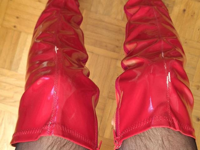 Bootsica-hot's shiny red patent leather boots, zipped up, showing her brown legs standing on a wooden floor. Boots are glossy and tight.