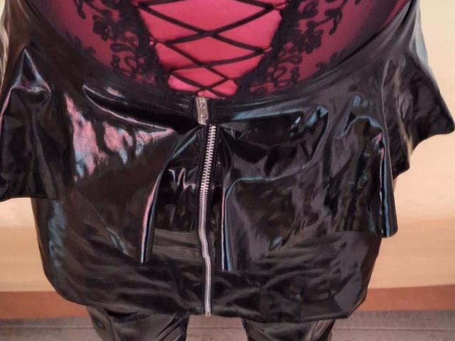 Bootsica-hot's black shiny leather skirt with a silver zipper, showing a red lace-up bodysuit underneath. Skirt is tight, flares out, and reflects light. Boobs and ass visible.