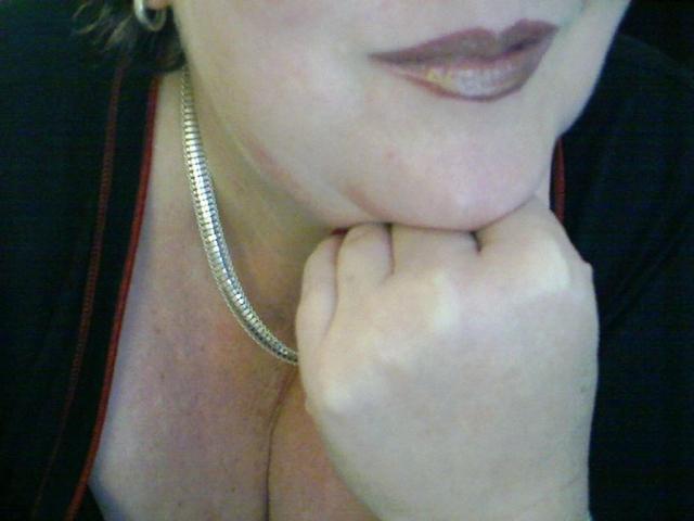 SECRET-CAM holds a white rose, wearing a silver necklace and white top, exposing her tits, with red nails and a silver watch, her face partially visible, smiling.