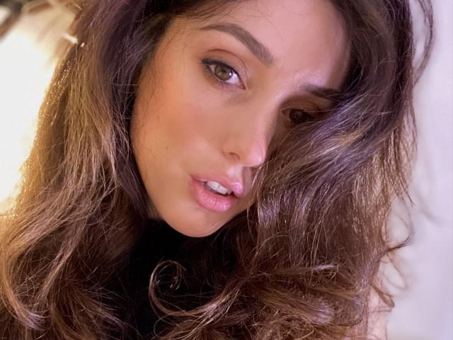 MiraDesire has long, wavy brown hair, brown eyes, and slightly parted pink lips. Her face is angled to the side with a soft, seductive look.