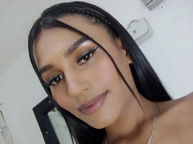SperanzaFoxy has long black braids, brown eyes, and full pink lips. She's wearing winged eyeliner and a silver necklace. Her smooth tan skin is visible.