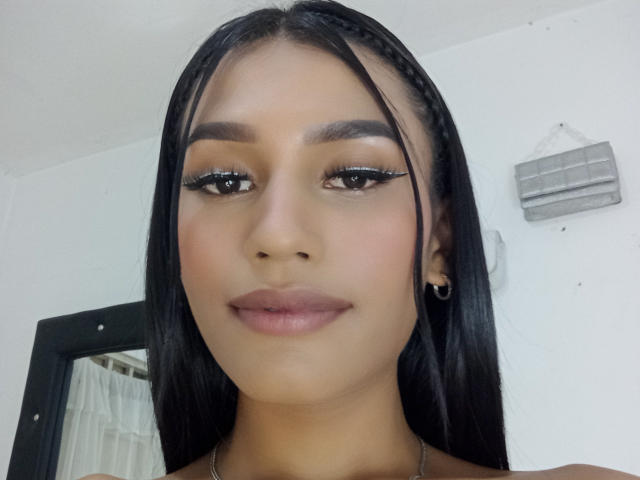 SperanzaFoxy has long black hair, brown eyes, and full lips with subtle makeup. She wears black eyeliner and small black earrings. Her skin is medium brown.