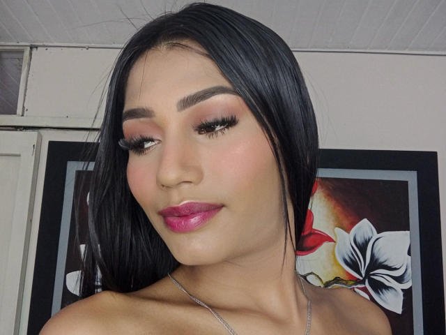 SperanzaFoxy with shiny black hair, pink lipstick, and thick eyelashes, showing off her pretty face and sexy smile, wearing a silver necklace, looking down.