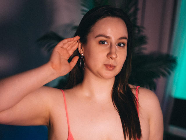 ViaLattea with wet brown hair, pink spaghetti strap top, small tits, fair skin, slightly pouty lips, hand touching ear, wearing hoop earrings, looking at camera.