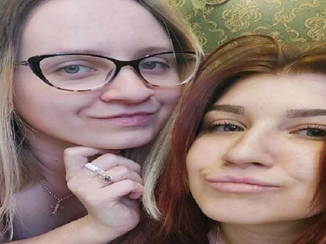 Two DoubleloveXXX-hots, one with glasses, blonde hair, and a ring, the other with red hair and a nose ring, smiling at the camera.