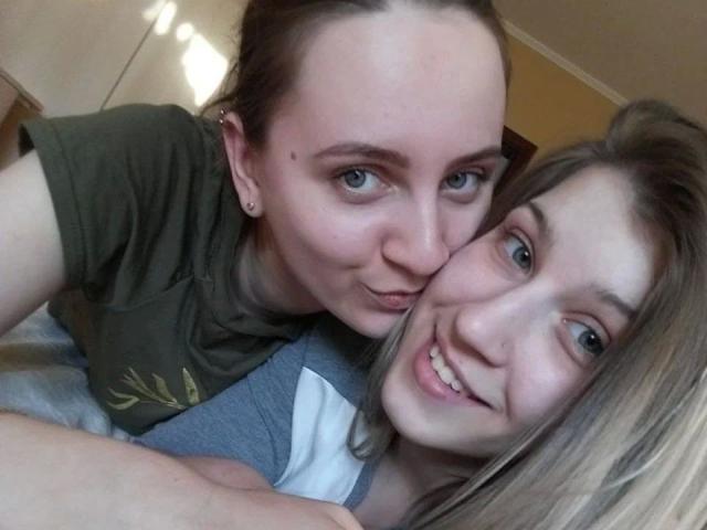 DoubleloveXXX-hot with short brown hair and green shirt leans over DoubleloveXXX-hot with long blonde hair and gray shirt, both smiling and showing cute, playful expressions.