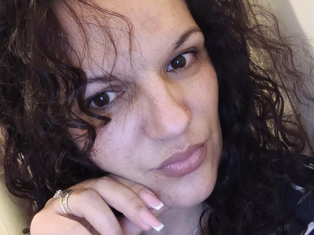 KissYouKissMe has curly black hair, brown eyes, light skin, and is looking at the camera with a slight smile. Her ringed finger rests on her cheek.
