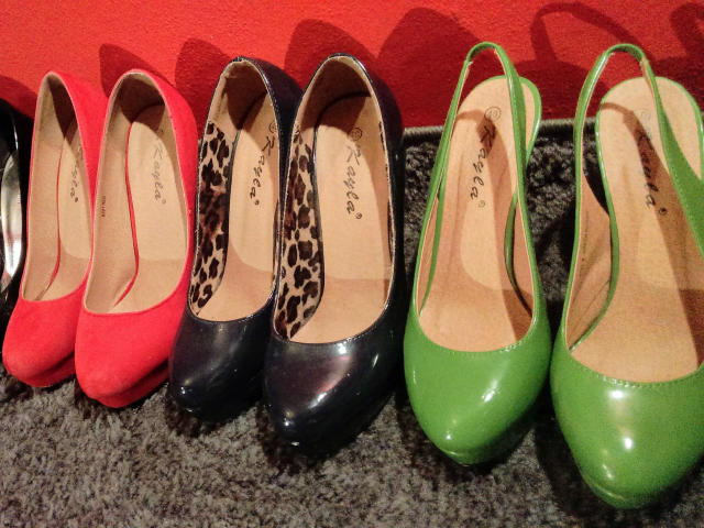 A row of shiny, glossy, high-heeled shoes: red, black with leopard print, and green, all lined up on a gray carpet. MistressOnline-hot's footwear collection.