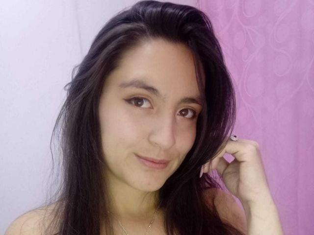 VenusSweetPalmer has dark, messy hair, brown eyes, and a slight smile. She's touching her hair with one hand, wearing a necklace, and has a cute, sexy face.