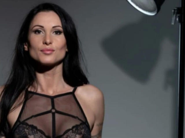 Elena Torres – attraktiv mit langen, schwarzen Haaren, trägt eine durchsichtige schwarze Spitzenbluse, die ihre Brüste zeigt. Sie hat ein leichtes Lächeln und einen sanften Schatten auf der rechten Seite..