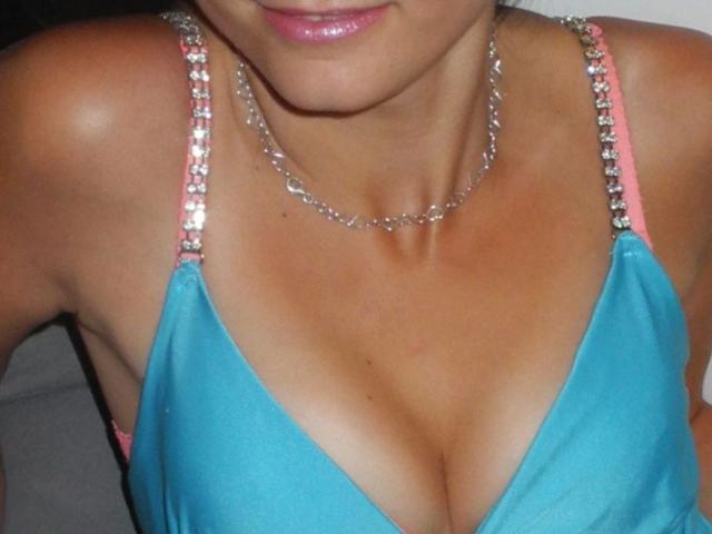 Il seno di Vicky-Acid-hot in un abito blu con spalline rosa e perline argentate, indossa una collana a catena d'argento, pelle abbronzata, labbra rosa, parte del viso visibile..