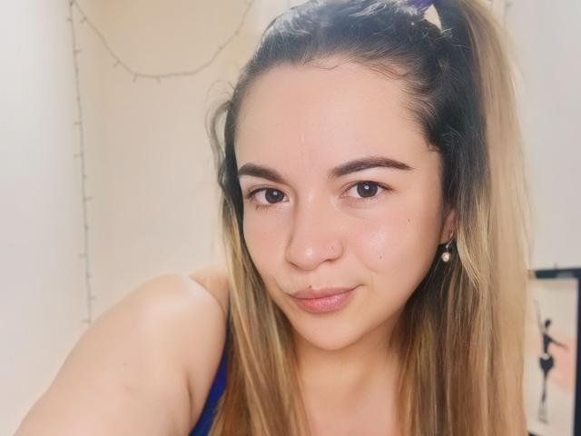 NaughtyCurvy heeft een lichte huid, bruine ogen en blond haar in een staart. Ze glimlacht, draagt een neusring en parel oorbellen, en heeft een blauwe top aan, waardoor haar borsten zichtbaar zijn..