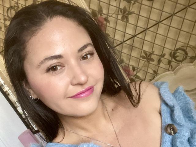 Hopeless has light brown skin, black straight hair, brown eyes, pink lipstick, small nose, and wears a blue off-shoulder top with a button. She's smiling slightly.