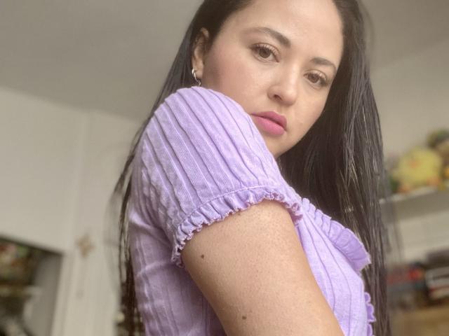 Hopeless with long black hair, wearing a purple ribbed top, showing her tits, pink lips, brown eyes, and earrings, in a soft-focused selfie.