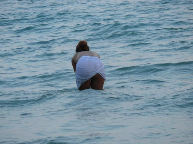 SubSandy-caliente, con las nalgas levantadas, agachada en agua azul, vestida con un trozo de tela blanca mojada que se adhiere a sus nalgas, con un moño de pelo castaño..