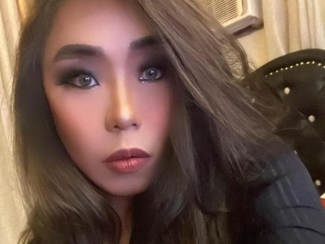 MissSultryAya has sultry brown eyes, full pink lips, and wavy brown hair. She's wearing black makeup and a black top, with a black tufted headrest in the background.