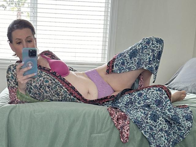 SkyChick lying on bed, wearing a leopard print robe, pink bra, and purple panties, holding a phone, showing her tits and pussy, in a relaxed, sexy pose.