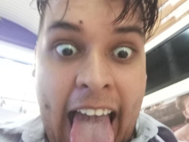 Bigchef's face, wide-eyed, with tongue out, looking goofy. He has a small mole on his left cheek and wet, dark hair. His mouth is open, showing his tongue.