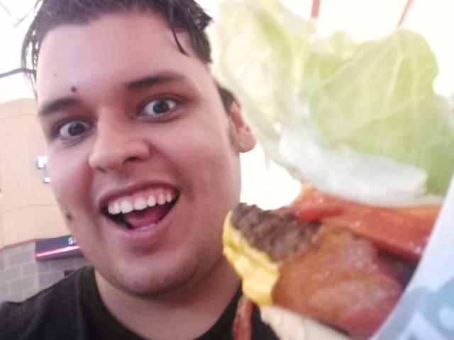 Bigchef has a surprised, open-mouthed expression, holding a burger with lettuce, cheese, and tomato. His dark hair is wet, and he's wearing a black shirt.