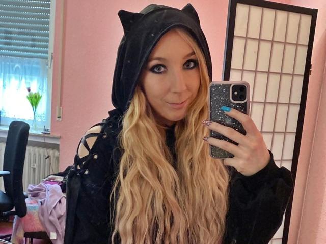 JustKerry-hot with long blonde hair, cat hood, black hoodie, and glittery phone, taking a mirror selfie, showing off cute eyes and subtle smile, with a slight pout.