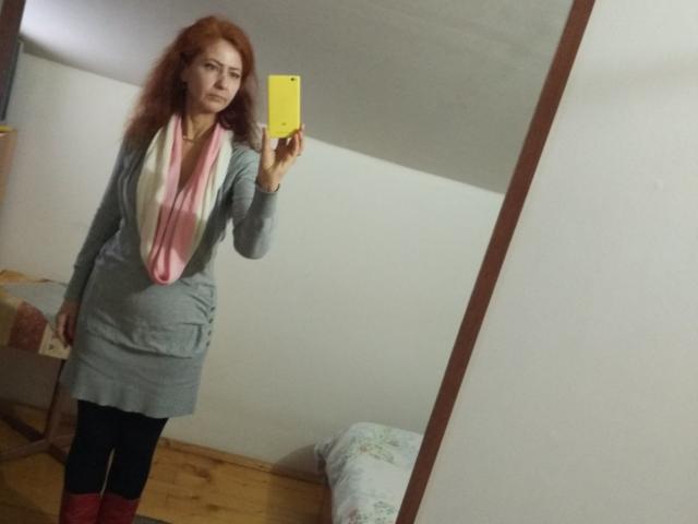 TaisieaViolet with red hair, wearing a gray dress, pink scarf, black leggings, and red socks, taking a mirror selfie with a yellow phone, showing her ass.
