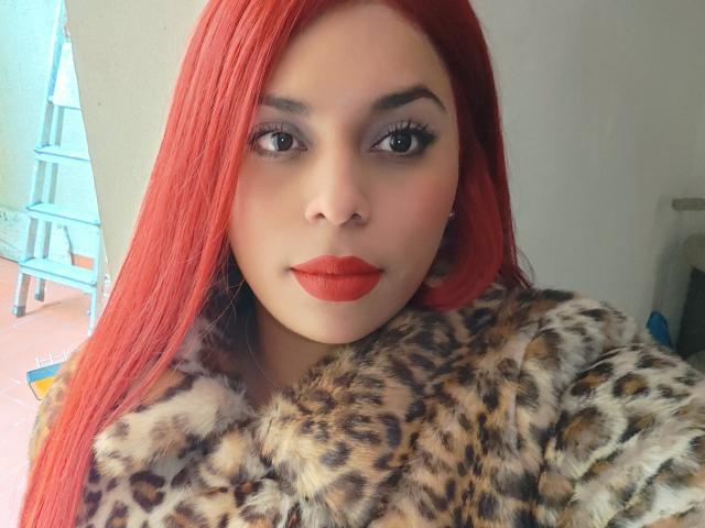 Chili aux cheveux rouge vif, rouge à lèvres rouge vif et manteau de fourrure léopard, regardant séduisante dans la caméra, son grand seins partiellement visibles.