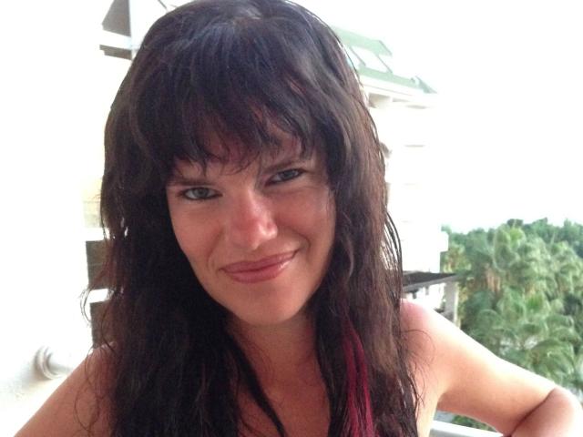 Jenny-Sun has wet, dark brown hair with pink highlights, small tits, and a cute smile. She's looking slightly to the side, with a relaxed, sexy expression.