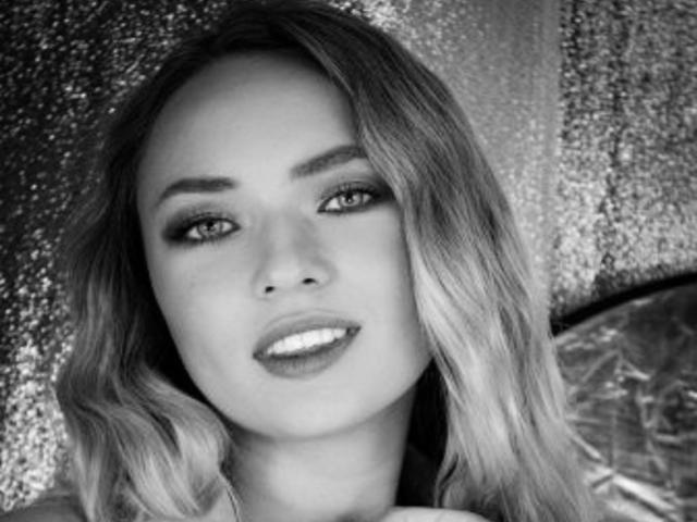 SallyVerda with wavy blonde hair, smoky eye makeup, glossy lips, and a slight smile, looking directly at the camera, in a black-and-white photo.