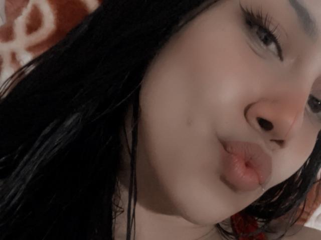 El rostro de Stephanie Davies, con cabello negro, labios carnosos ligeramente fruncidos como si estuviera besando, largas pestañas y una leve sonrisa, que resaltan sus rasgos lindos, sensuales y atractivos..