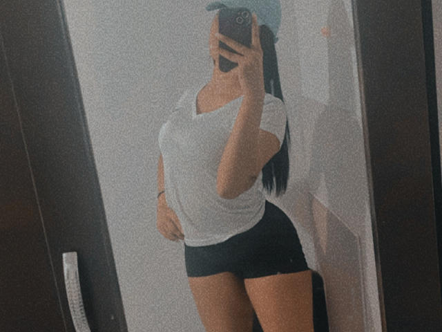 StephanieDavies with a white tee, black shorts, and a blue cap, taking a mirror selfie, showing off her big ass and small tits, holding a phone in her hand.