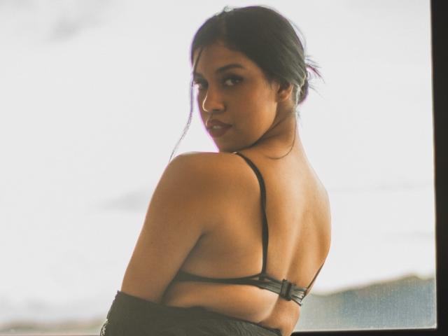 StephanieDavies with her back to the camera, looking over her shoulder, wearing a black bra, her tits visible, dark hair in a loose bun, soft light, slightly overexposed.