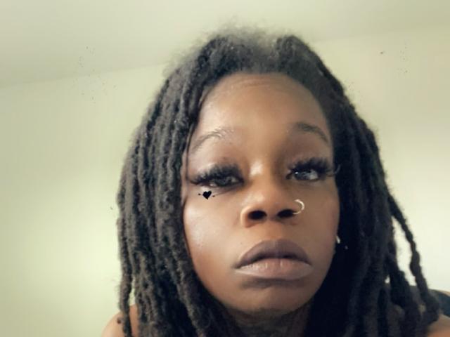A JessyXBabe69 tem a pele marrom escura, cabelos longos trançados em dreadlocks, um piercing no nariz e uma pequena tatuagem de um coração preto perto do olho direito. Seus lábios cheios estão ligeiramente entreabertos..